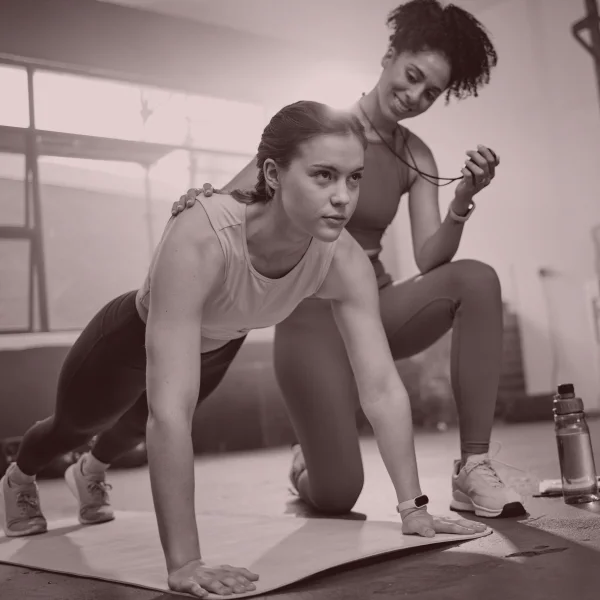 Deux femmes effectuant des pompes dans une salle de sport, guidées par un entraîneur privé