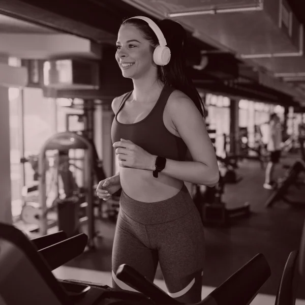 Une femme s'entraîne sur un tapis de course dans une salle de sport, concentrée sur son exercice physique.