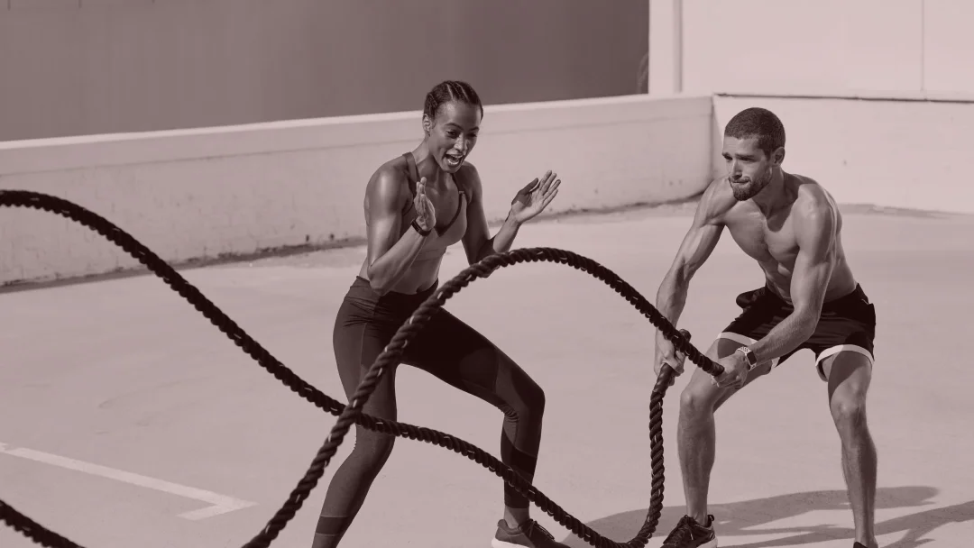 Deux personnes s'entraînent avec des cordes de combat en plein air, guidées par un entraîneur privé.